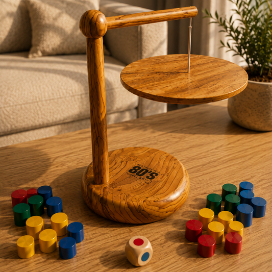 A wooden balance game set on a light wood table in a living room setting. The set includes a circular wooden base with a printed logo, a vertical wooden support, a round wooden platform with a hanging string, and multiple small colorful cylindrical pieces in red, yellow, and blue scattered around.
